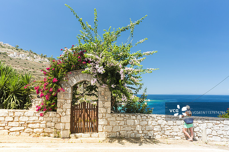 游客在花团锦簇的门廊附近欣赏利梅尼村，希腊伯罗奔尼撒马尼地区利梅尼图片素材