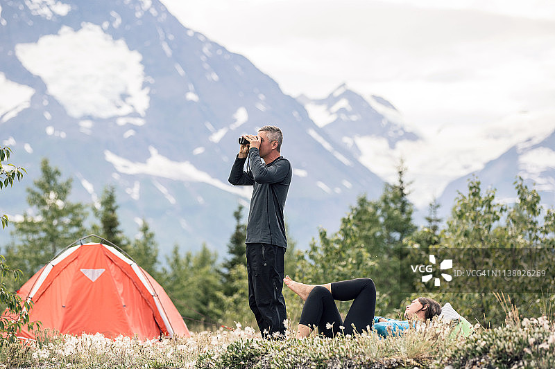荒野露营情侣，男性伴侣正在使用双筒望远镜图片素材