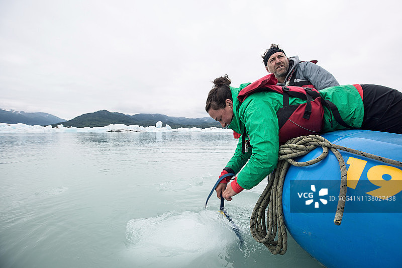 女人从木筏上探出身子，从泻湖中拉出一块冰图片素材