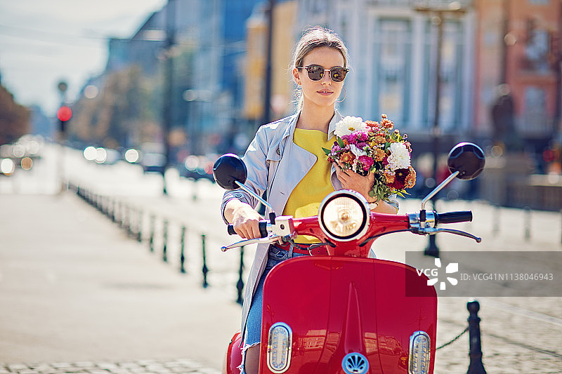 在城市里骑滑板车的抱着鲜花的年轻女孩图片素材