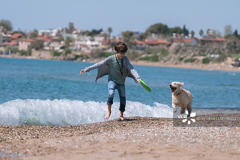 快乐男孩在海滩上和他的狗一起奔跑图片素材