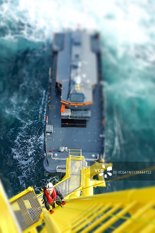 使用绳索进入技术的工人攀爬塔式天线，使用挂钩并查看相机图片素材