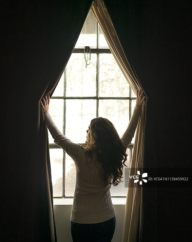 打开窗帘的年轻女人图片素材