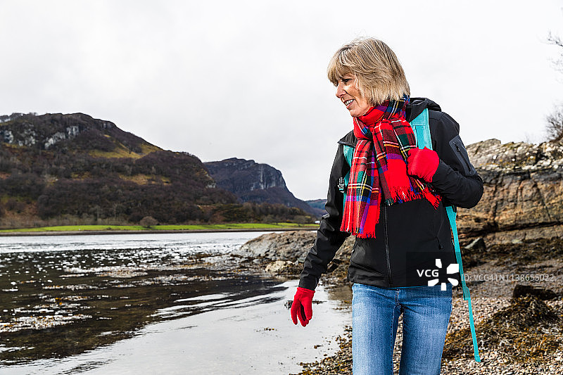 年长的妇女在春日里沿着卵石海滩散步图片素材