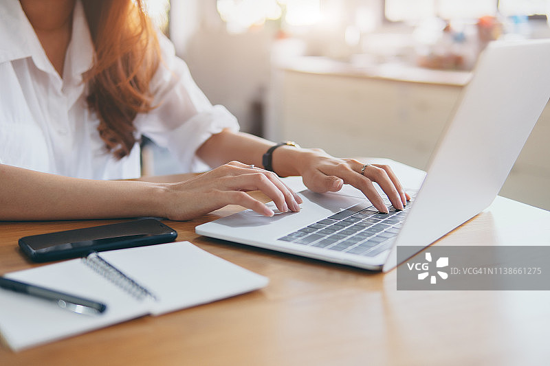 女人用笔记本电脑工作。双手使用数字技术工作。在办公桌环境下工作。使用移动设备和笔记本电脑进行金融技术规划。图片素材