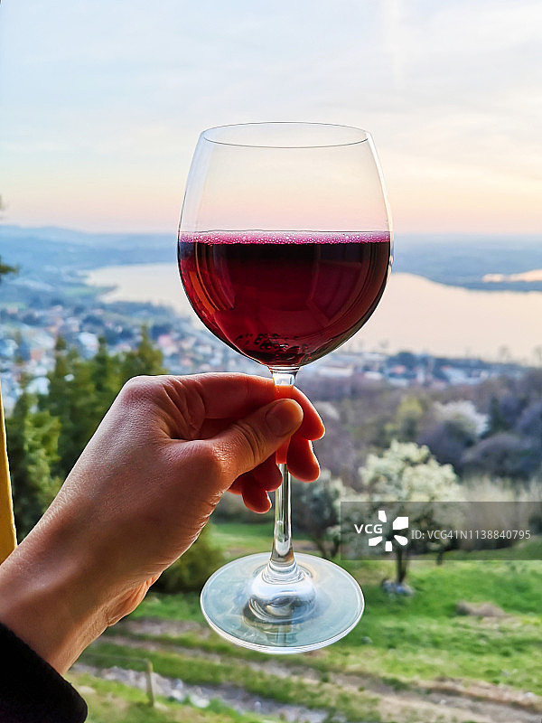 手持红酒杯，背景为日落湖面图片素材