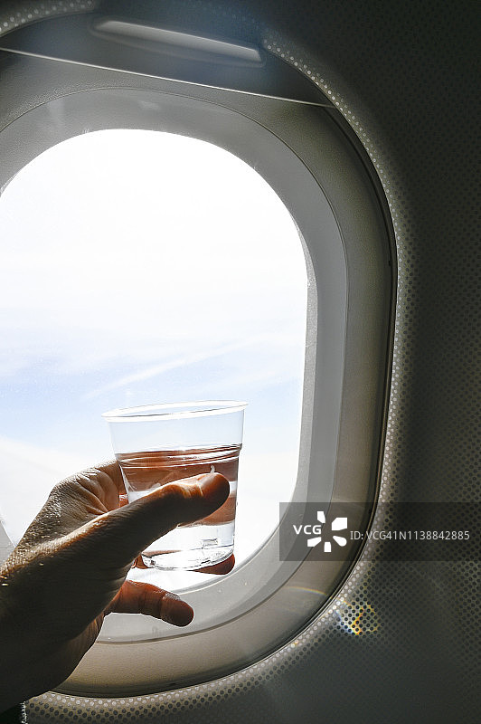 男子手持一杯水，在飞机舷窗前图片素材