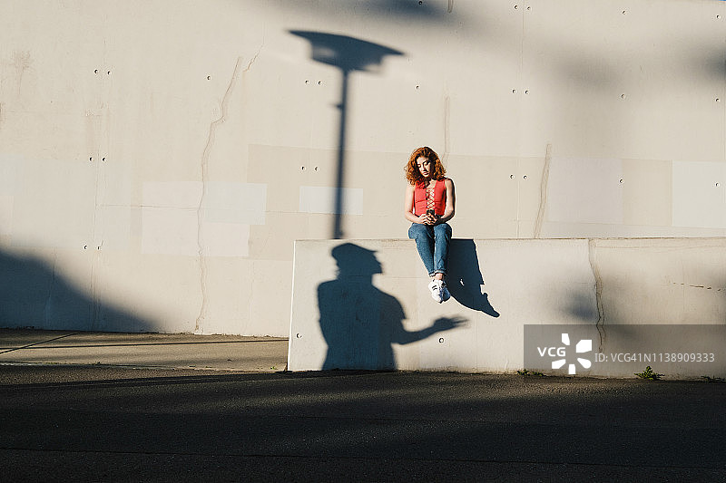 城市墙壁上使用智能手机的年轻女人的阴影图片素材