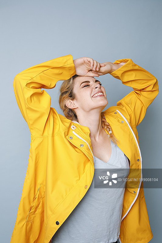 快乐的年轻女子在蓝色背景前穿着黄色雨衣图片素材