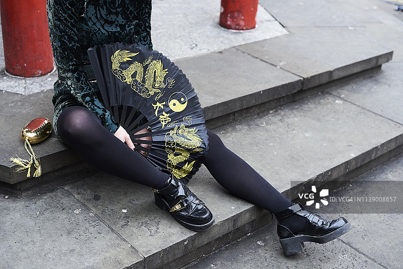 伦敦唐人街：一位年轻女子手持中国风扇坐在台阶上图片素材