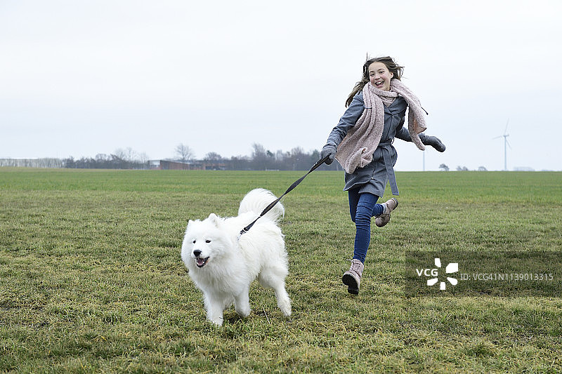 在草地上和她的狗一起奔跑欢笑的女孩图片素材