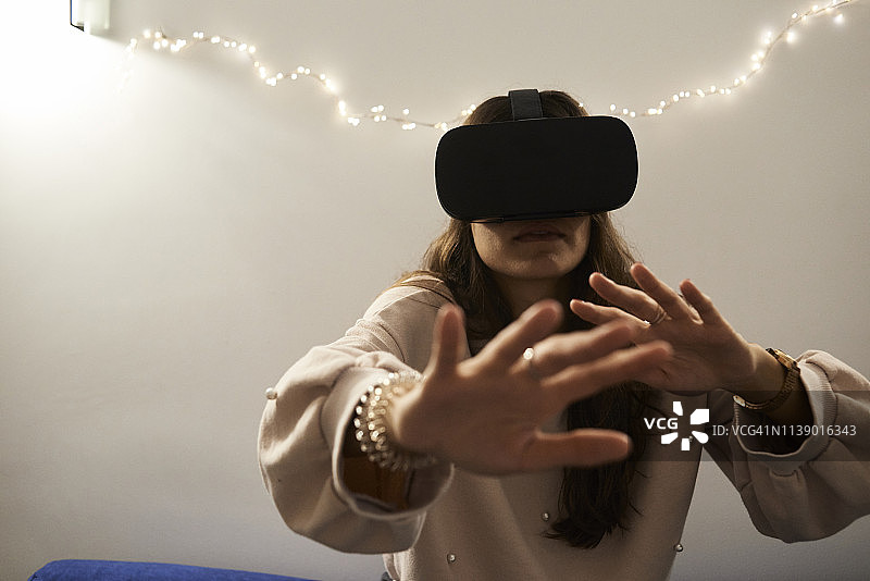 年轻女人晚上在家里的沙发上使用VR头显玩游戏图片素材