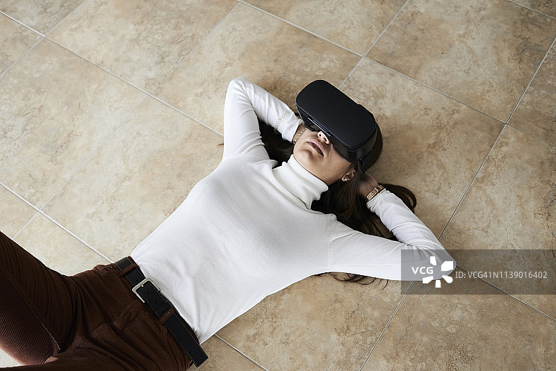 在家躺在地板上使用VR头显的年轻女人图片素材