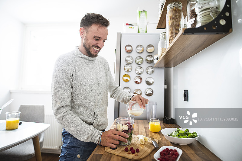 年轻白人男子在厨房准备健康的水果早餐图片素材