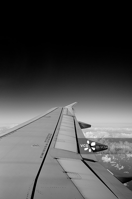 黑白云层之上飞行中的飞机机翼图片素材