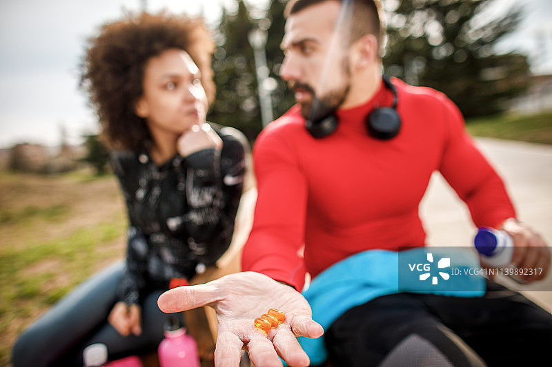坐在公园长椅上，手 holding 橙色胶囊的健壮男人图片素材