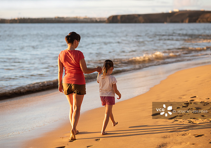 母亲和女儿在海滩上散步的背影图片素材