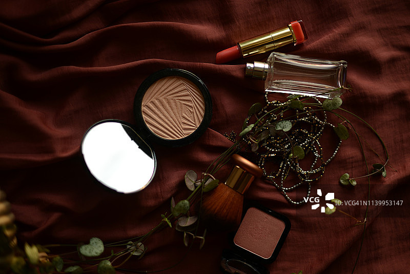 深色丝绸背景上的口红、粉饼、腮红、项链和香水瓶图片素材