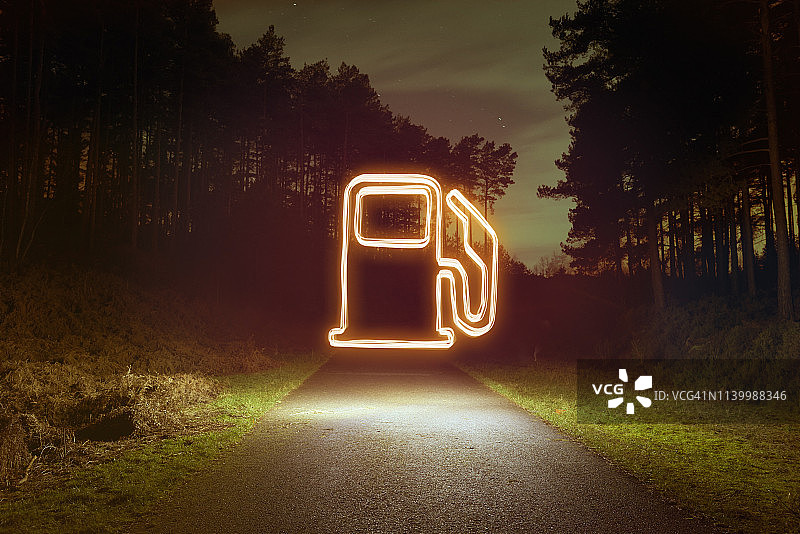 夜晚森林道路上方的发光加油泵标志图片素材