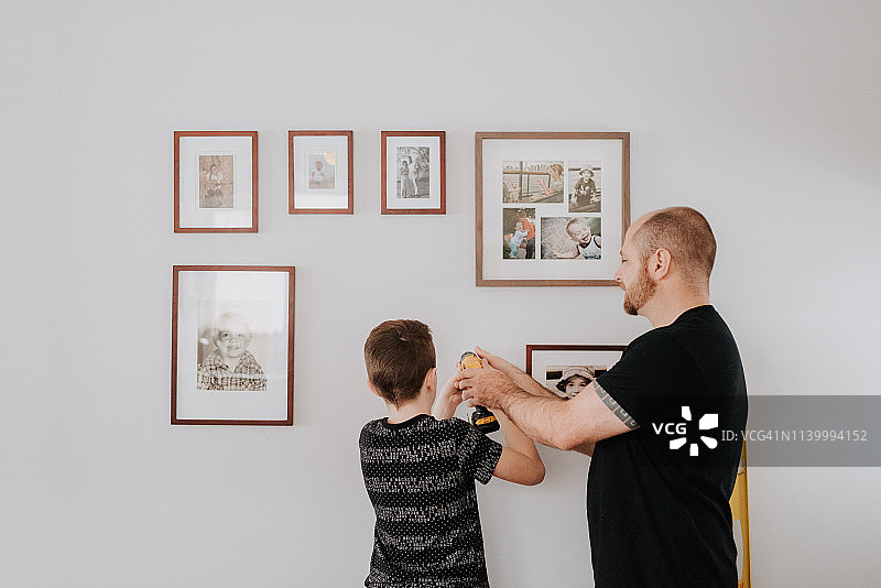 父亲教儿子用钻头在墙上打孔，安装相框图片素材