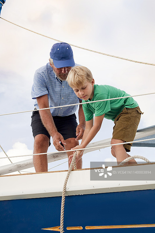 男孩帮助祖父在帆船上拉绳索图片素材