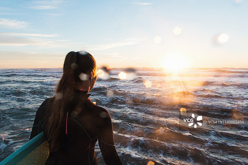 日落时分在加利福尼亚卡迪夫海边涉水的女性冲浪者背影图片素材