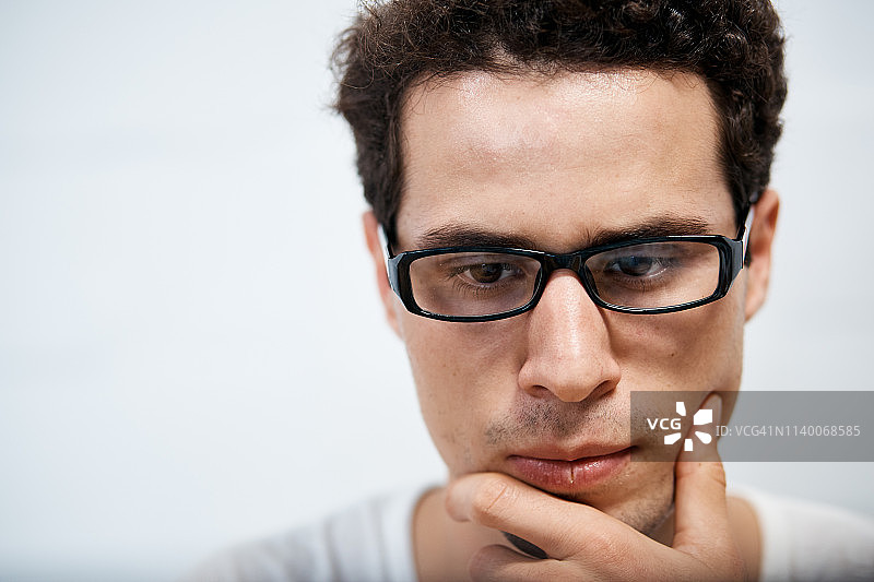 戴眼镜、手托下巴、若有所思的年轻男子图片素材