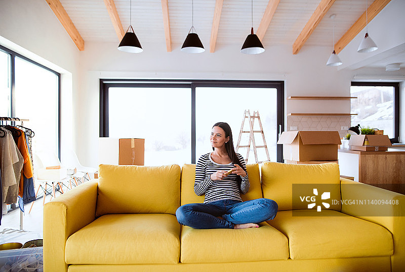 新家客厅里坐在黄色沙发上的年轻女子图片素材