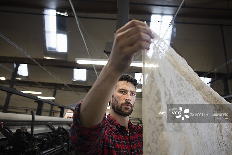 纺织厂里，男织布工检查旧织布机上的花边布的肖像图片素材