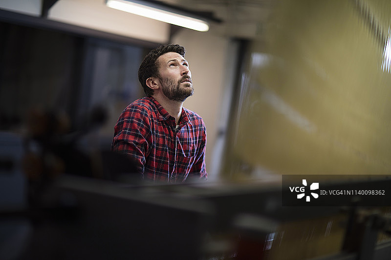 在纺织厂看着旧织布机上线的年轻男性织布工图片素材