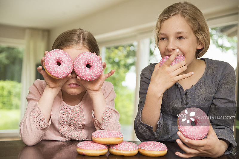 姐妹俩，一个用甜甜圈遮住眼睛，另一个在吃东西图片素材