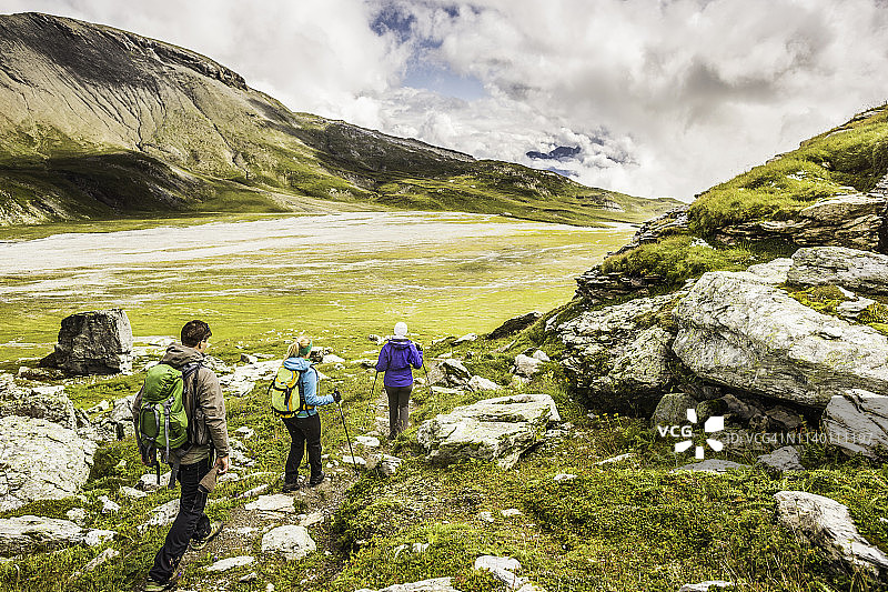 沿着小路徒步旅行的三名徒步旅行者的背影，瑞士格劳宾登Segnesboden图片素材