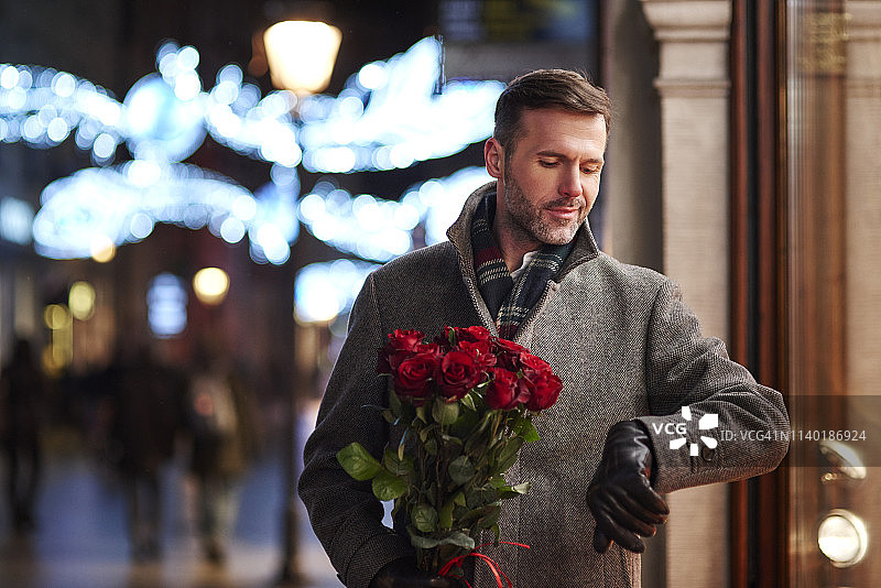 手捧红玫瑰看时间的等待男子肖像图片素材