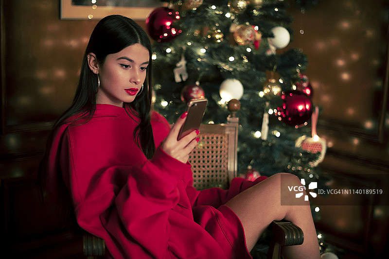 坐在圣诞树前看手机的少女肖像图片素材