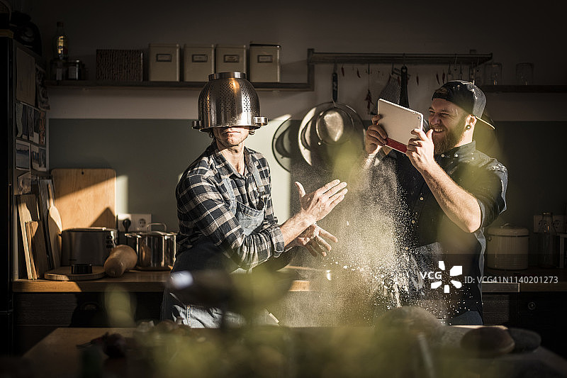 年轻男人拍摄在厨房戴滤锅当头盔的朋友图片素材