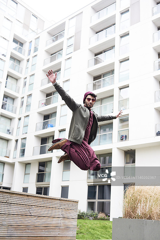 戴紫色帽子和印度服装的时尚男人跳过现代建筑图片素材