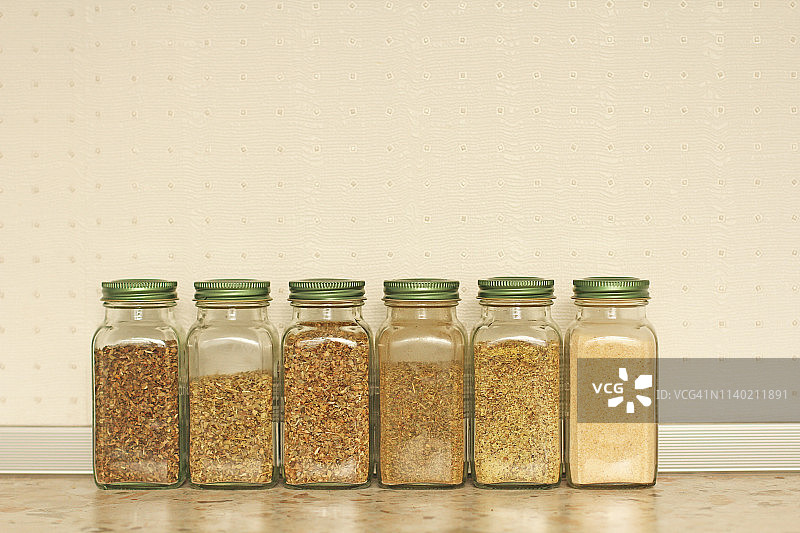 厨房浅色背景上的玻璃罐装香料：罗勒、牛至、意大利香草，带文本复制区图片素材