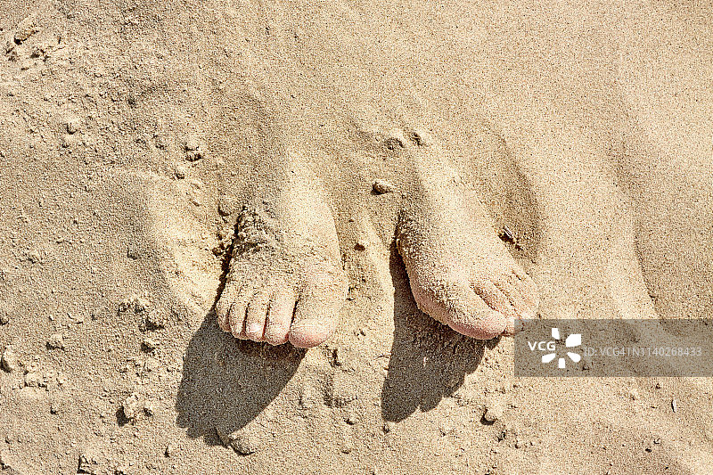 儿童的双脚从沙滩中伸出图片素材