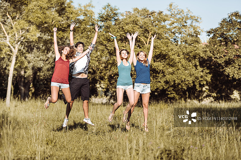 快乐的青少年在公园里举起手臂跳跃图片素材