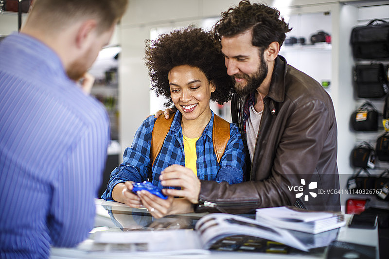 在相机店店员的帮助下，情侣购买小型蓝色卡片相机图片素材