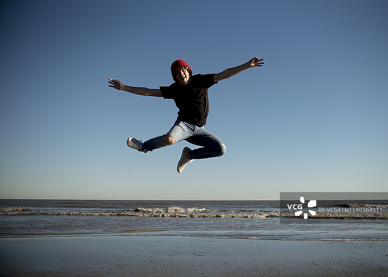 快乐的青少年男孩在美国得克萨斯州加尔维斯敦的海滩上跳跃图片素材