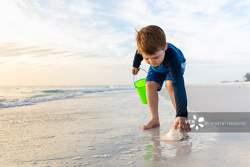 孩子弯腰捡海滩上的贝壳图片素材