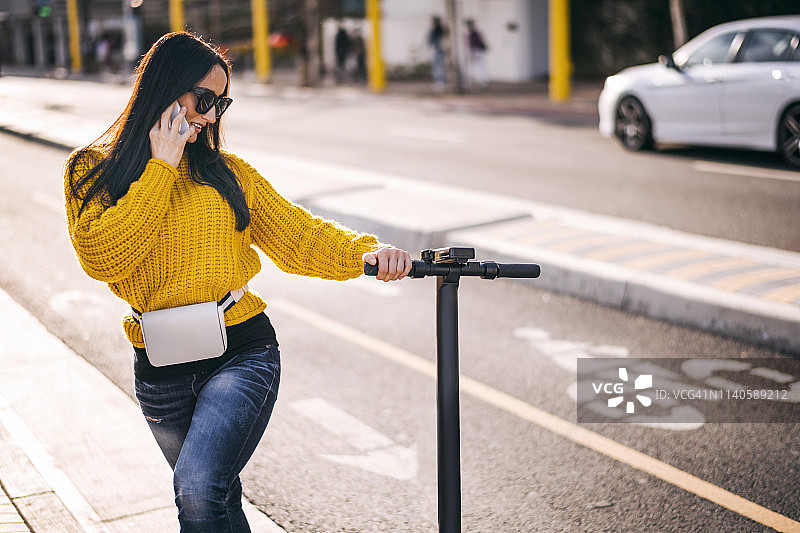 在市中心手持电动滑板车打电话的现代女性图片素材