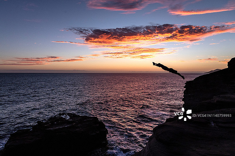 日落时分从悬崖跳入海洋的潜水员图片素材