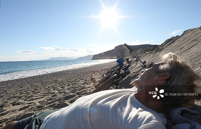 夕阳下，中年男人在海滩上放松骑自行车图片素材
