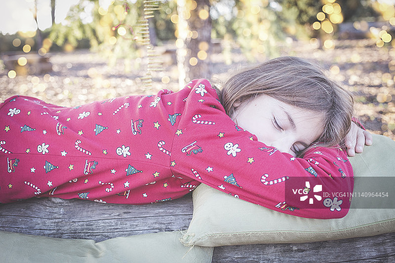 男孩穿着圣诞节睡衣在西班牙花园的木头上睡觉图片素材