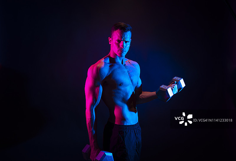 黑色背景下举哑铃的健壮男人图片素材