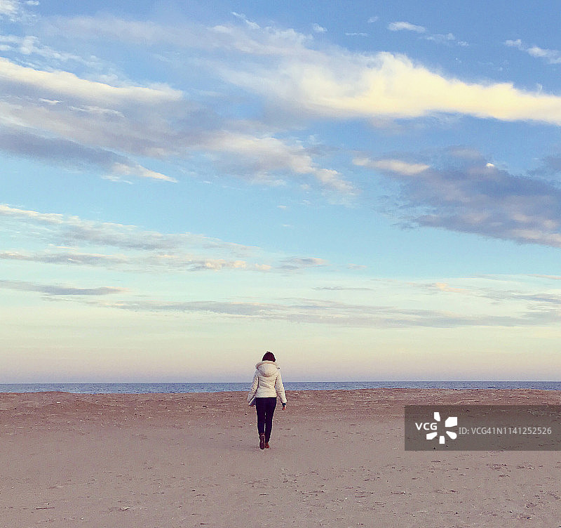 女孩在黄昏时分走在荒凉的冬季海滩上图片素材