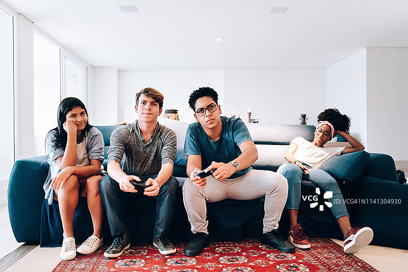 一群年轻的青少年朋友在家玩电子游戏，女孩们感到无聊图片素材