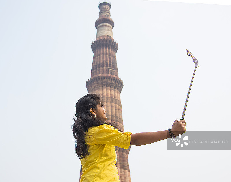 在印度德里顾特卜塔前用自拍杆自拍的年轻女子图片素材